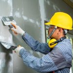 Worker repairs wall,Construction industry worker using a putty knife and leveling in house under reconstruction.